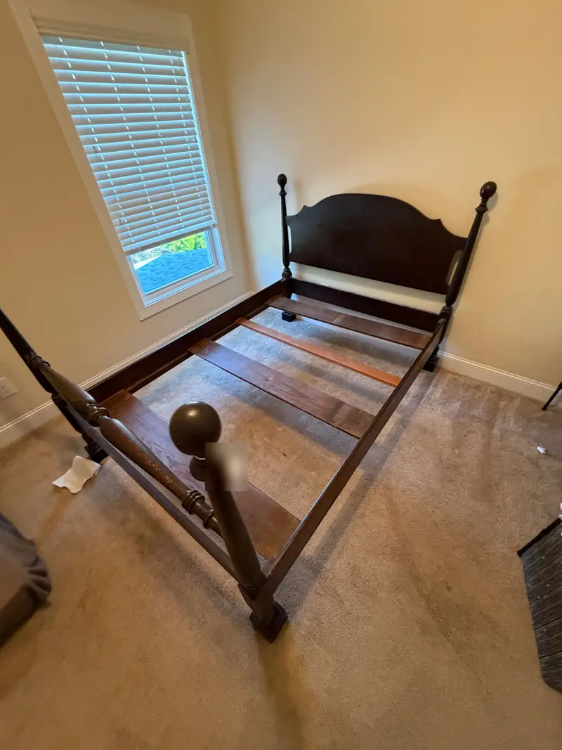A dark wooden four-poster bed frame with its slats in place in an empty bedroom.