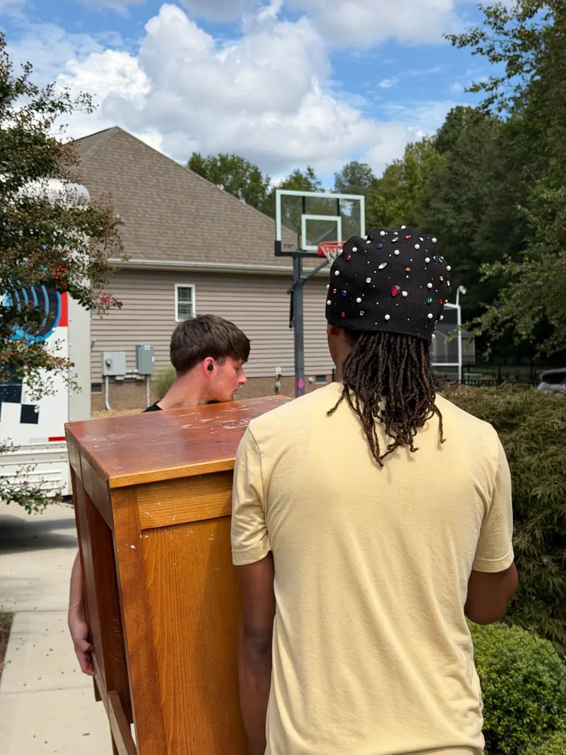 Two movers carrying a wooden dresser along a walkway toward the truck.
