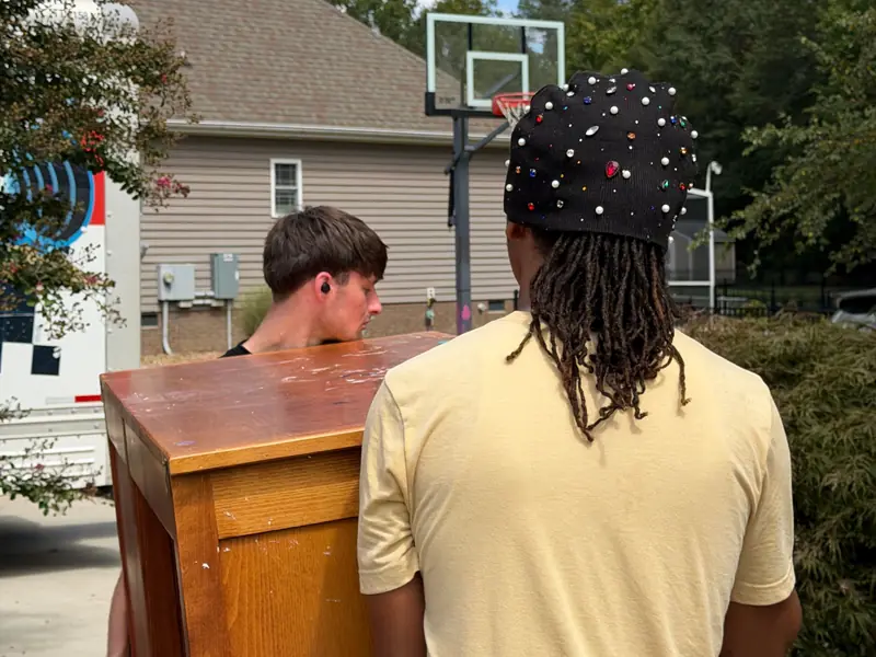 Two movers carrying a wooden dresser along a walkway toward the truck.