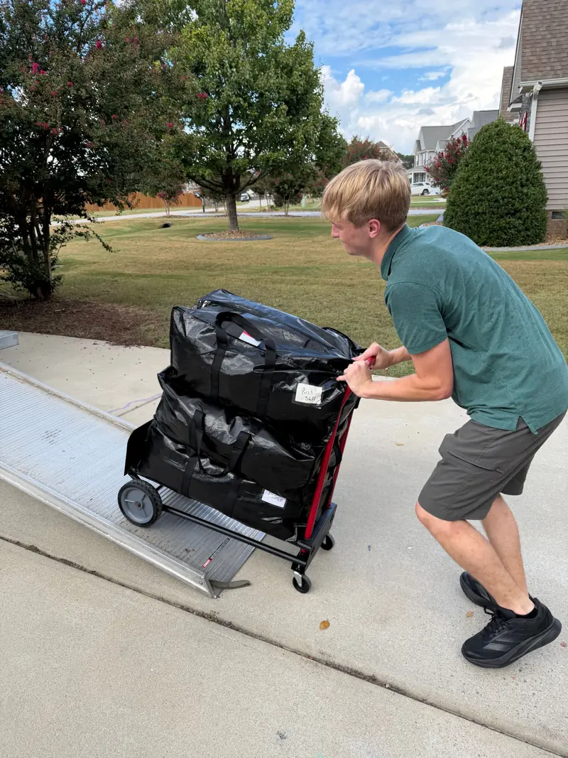 A mover wheeling three stacked moving bags on a hand truck toward a rental truck ramp.