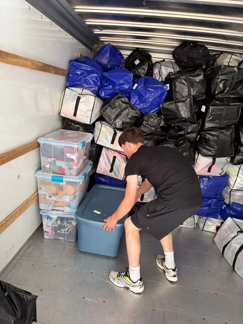 A mover sliding a storage tote into place beside clear plastic bins inside a rental truck.