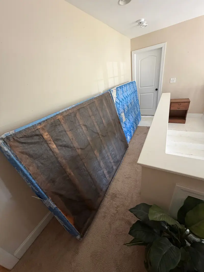 A box spring and mattress standing against a hallway wall.