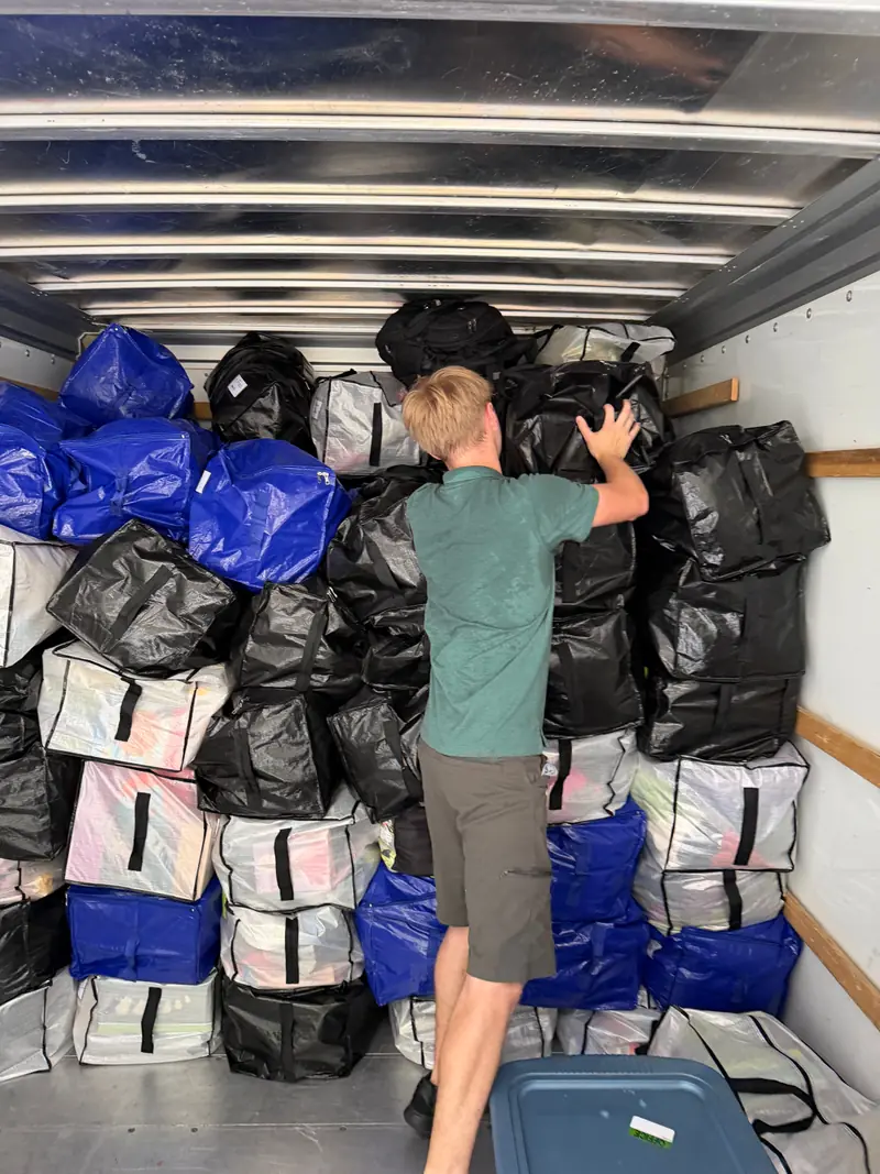 A mover stacking black, blue and white moving bags into a tight wall inside a rental truck.