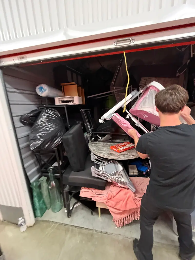 A mover lifting folded chairs out of a packed self-storage unit.