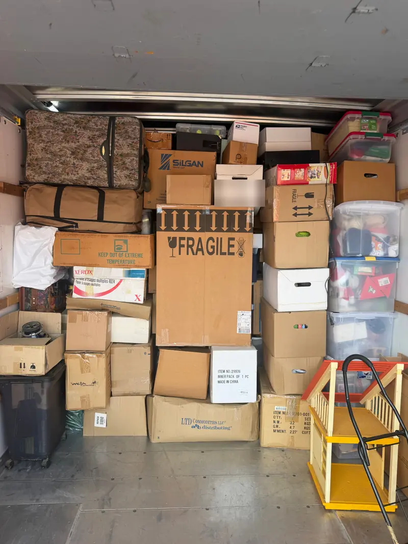 Boxes, suitcases and storage totes stacked floor to ceiling inside a rental truck, with a large box marked fragile in the middle.