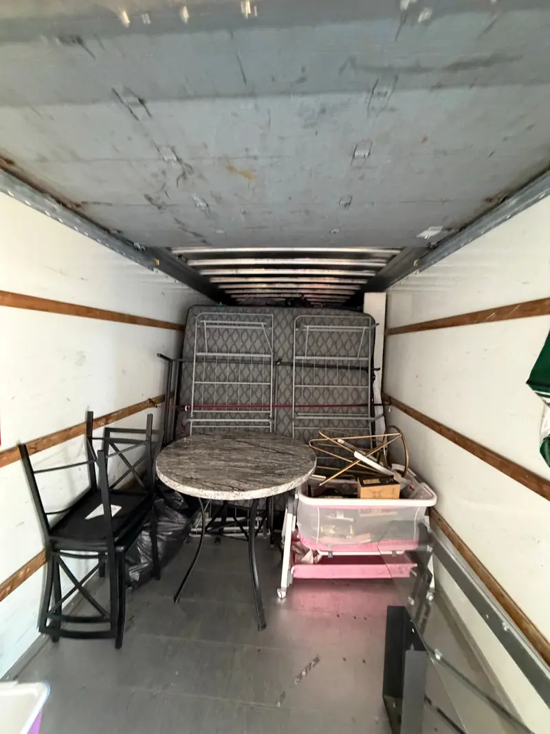 A round stone-top table, black chairs and a bed frame loaded at the front of a rental truck.